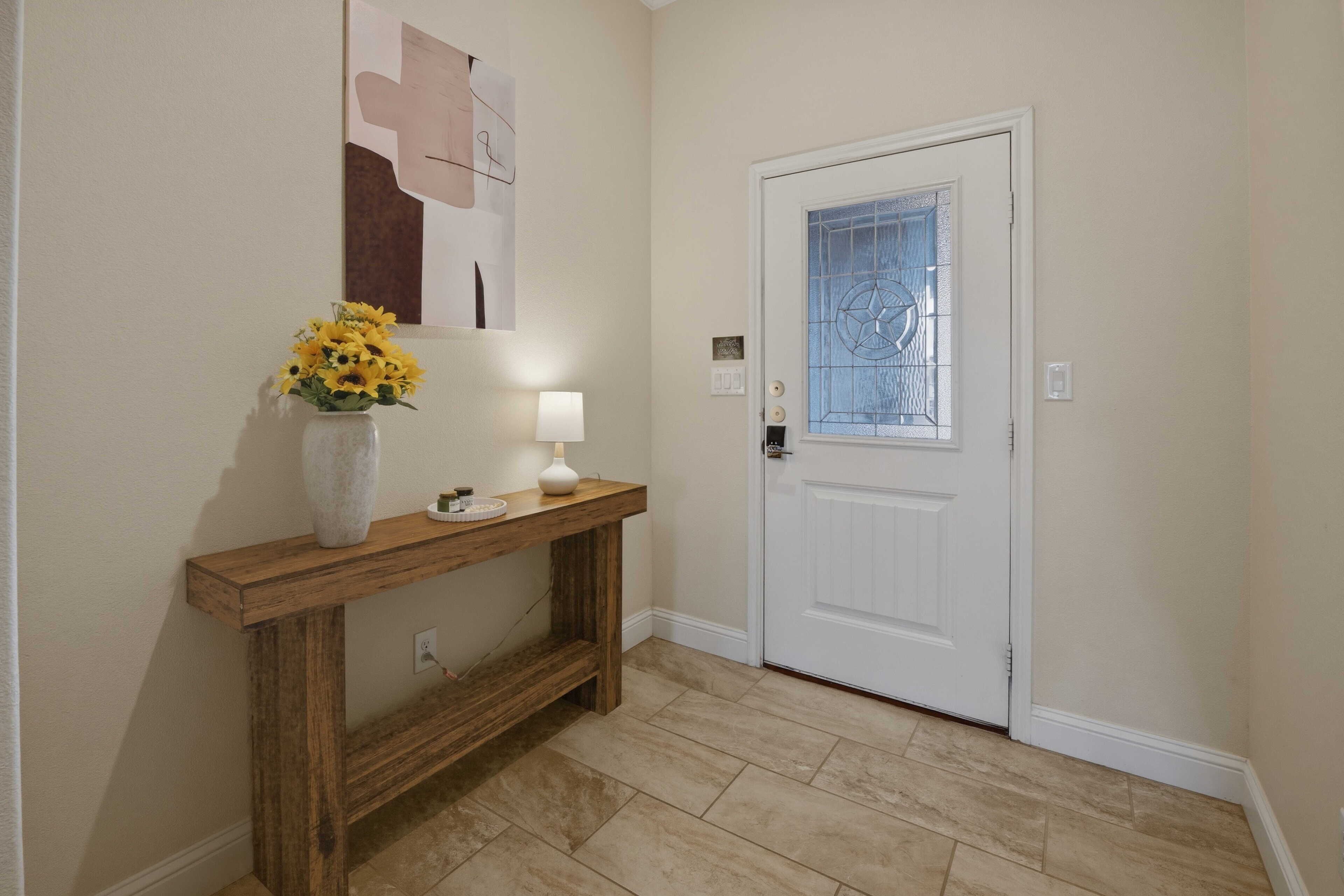 A hallway with a wooden console table, a vase of yellow flowers, a white lamp, and a door with a glass panel.
