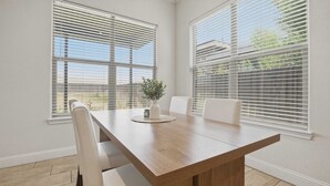 Un comedor con una mesa de madera, sillas blancas y un jarrón con una planta.