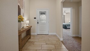 A hallway with a white door, a wooden console table with a lamp, and a vase of flowers. - Corporate Housing - Midland TX - ACOMM (Midland)