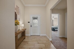 Un pasillo con una puerta blanca, una consola de madera con una lámpara y un jarrón de flores.