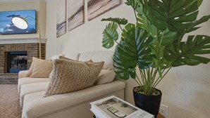 Una sala de estar con un sofá, una planta en maceta, una revista y un televisor en la pared.