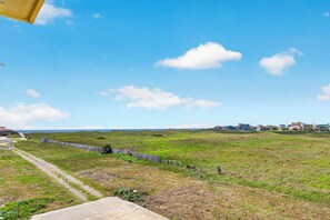 A grassy field with a fence, a clear sky, and distant buildings. - Luxe 2BR: Boardwalk + 3rd Floor Deck (Port Aransas)