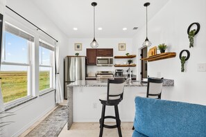 A modern kitchen with a central island, bar stools, and a blue sofa.