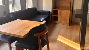 A modern living space with a sofa, a wooden dining table, and a built-in wooden shelving unit. - Hotel Karakoy Corner Port (İstanbul)