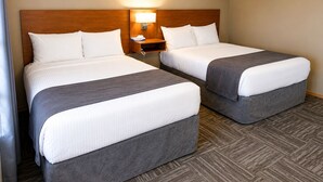 A hotel room with two beds, a nightstand with a lamp, and a herringbone-patterned floor. - Ste Anne Hotel (Ste Anne)