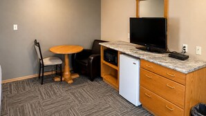 A compact room with a wooden cabinet, a television, a small refrigerator, a round table, and a chair. - Ste Anne Hotel (Ste Anne)