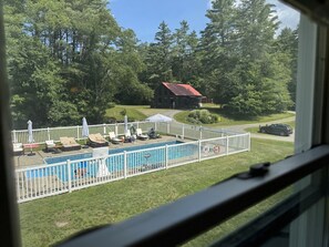 A view of a swimming pool with lounge chairs and umbrellas, surrounded by a white fence, with a building and trees in the background. - The Landgrove (Londonderry)