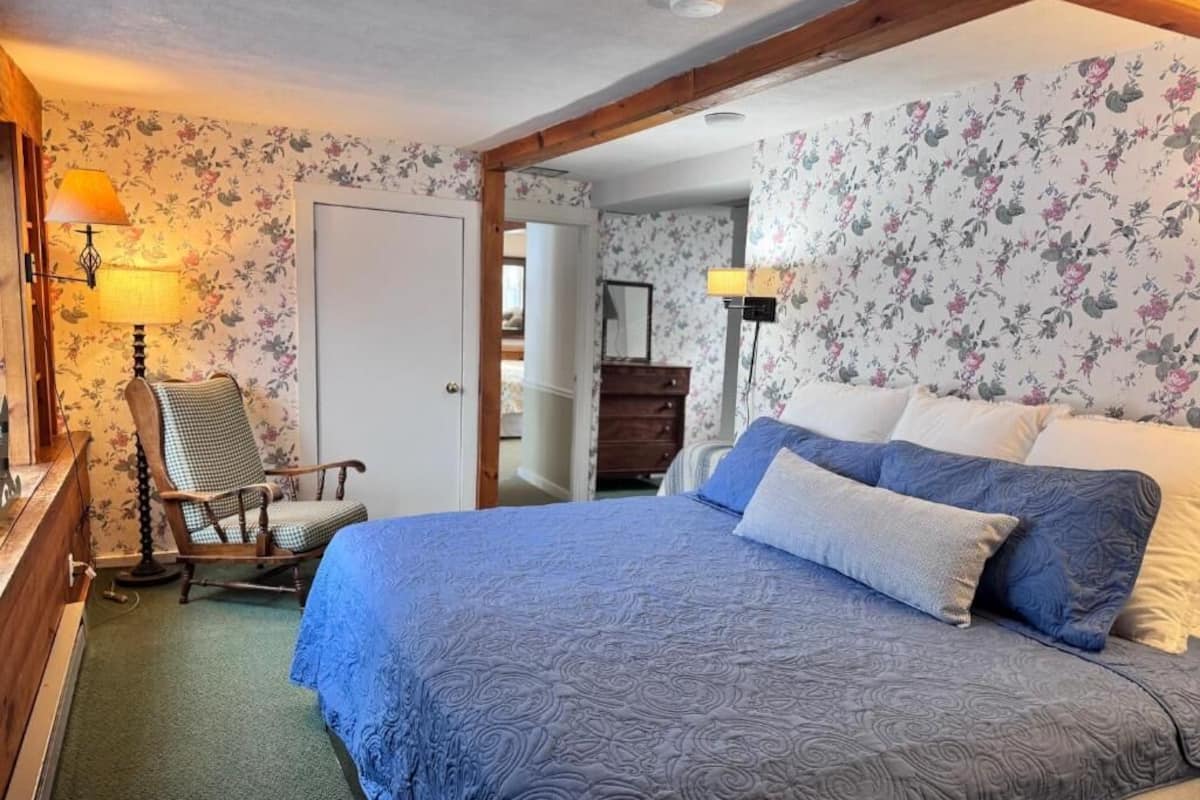 A bedroom with a bed, a chair, a dresser, and a lamp.