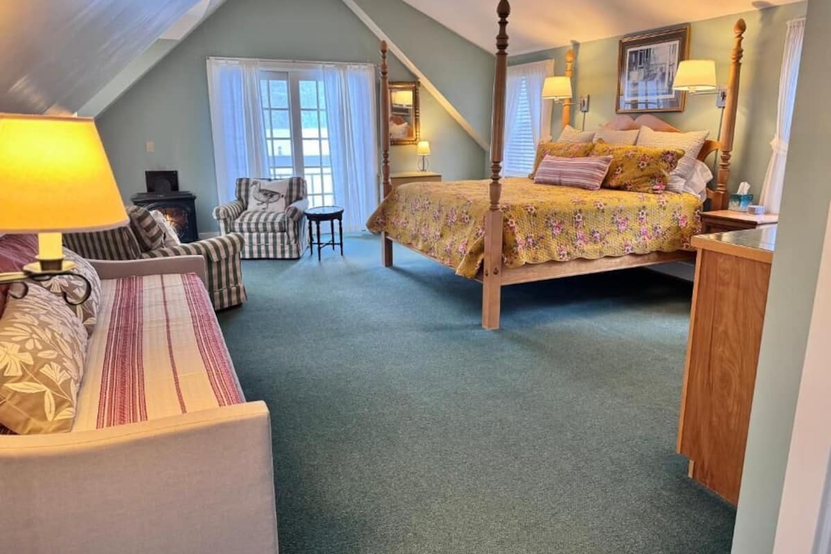 A bedroom with a four-poster bed, a chair, a desk, and a window with curtains.