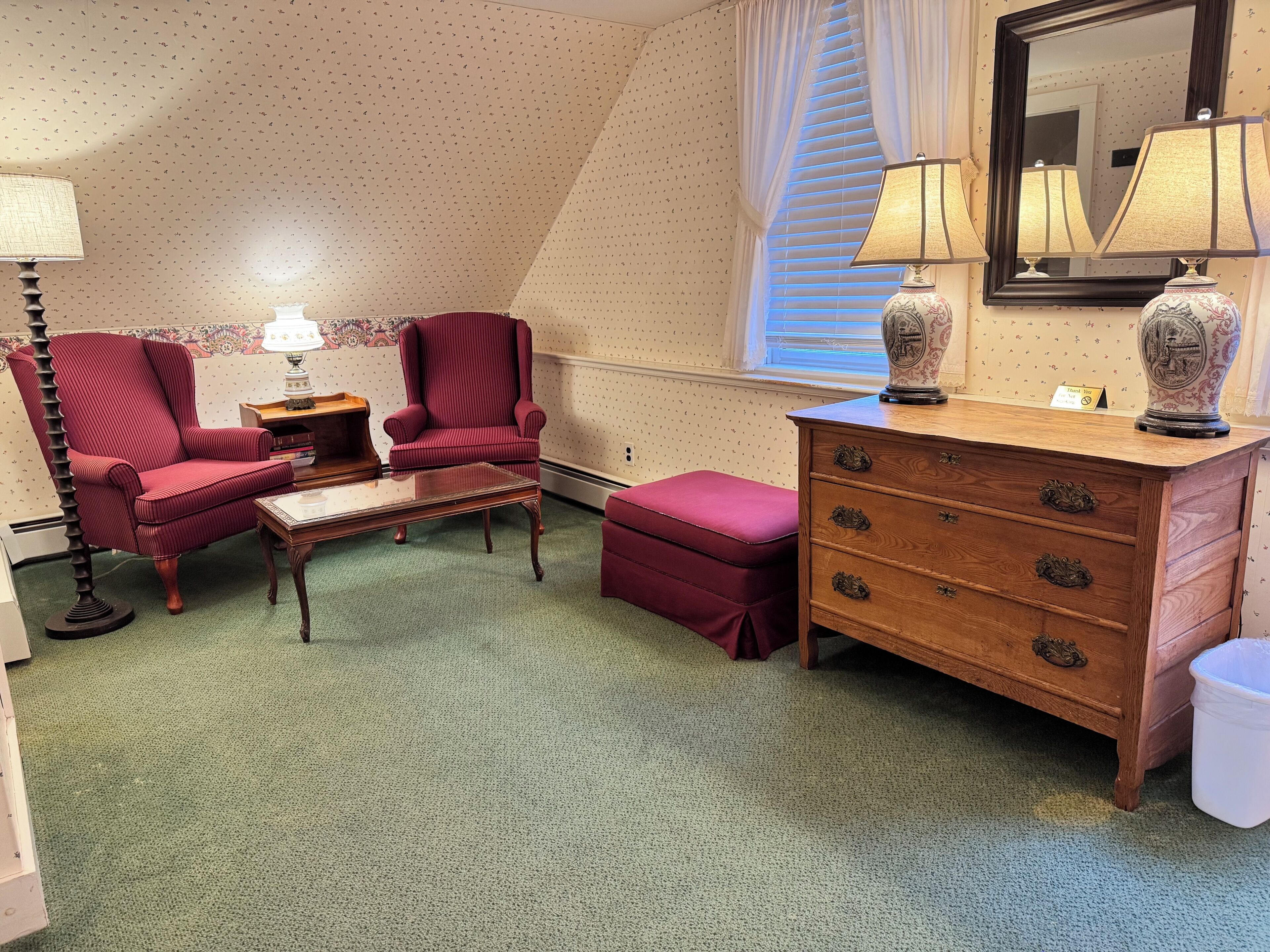 A room with a red armchair, a wooden dresser, a mirror, and a window with blinds.