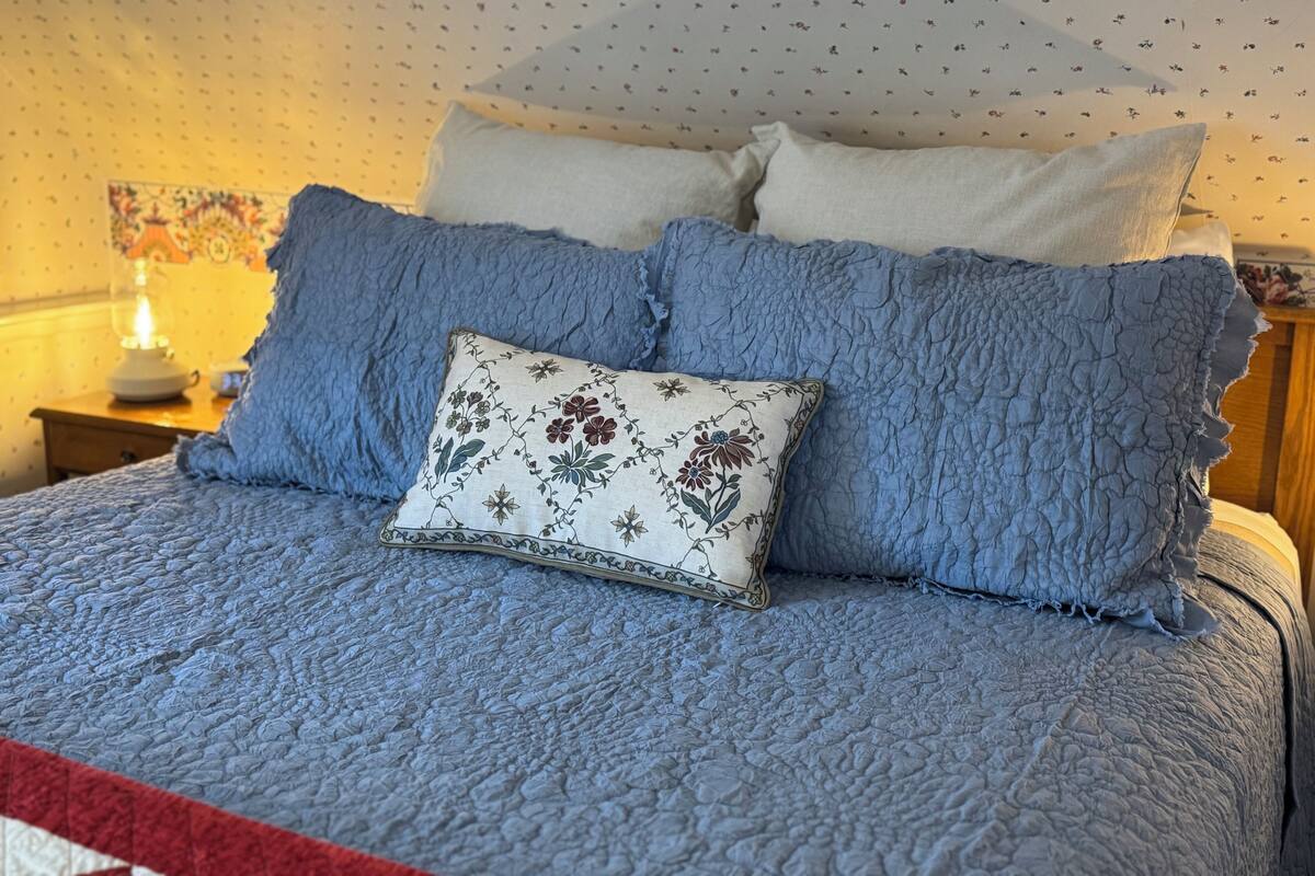 A bed with a blue quilt, a floral pillow, and a white pillow.