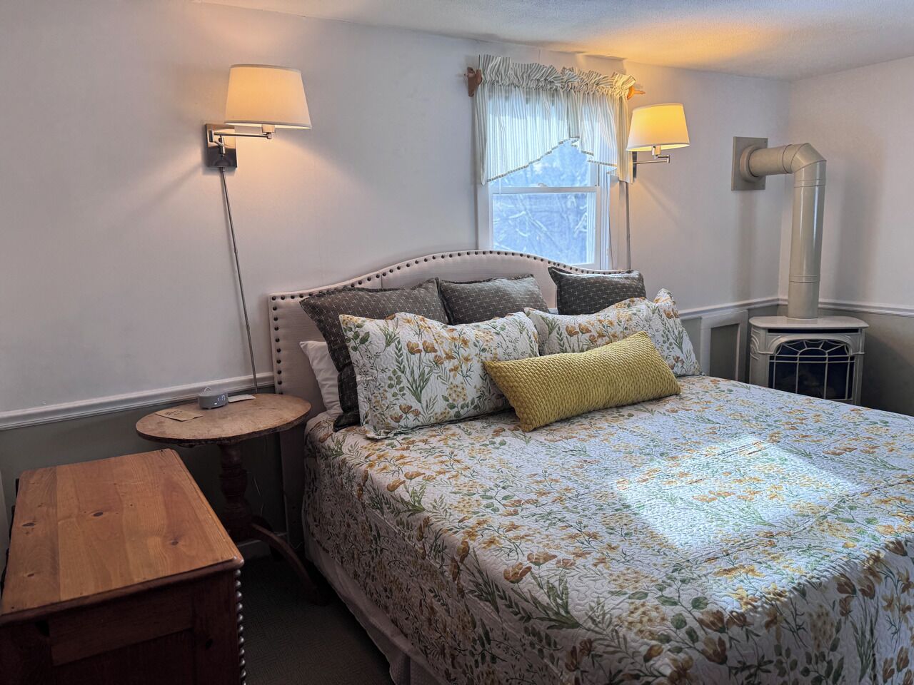 Une chambre à coucher avec un lit, des lampes de chevet, une table ronde et une fenêtre avec des rideaux.