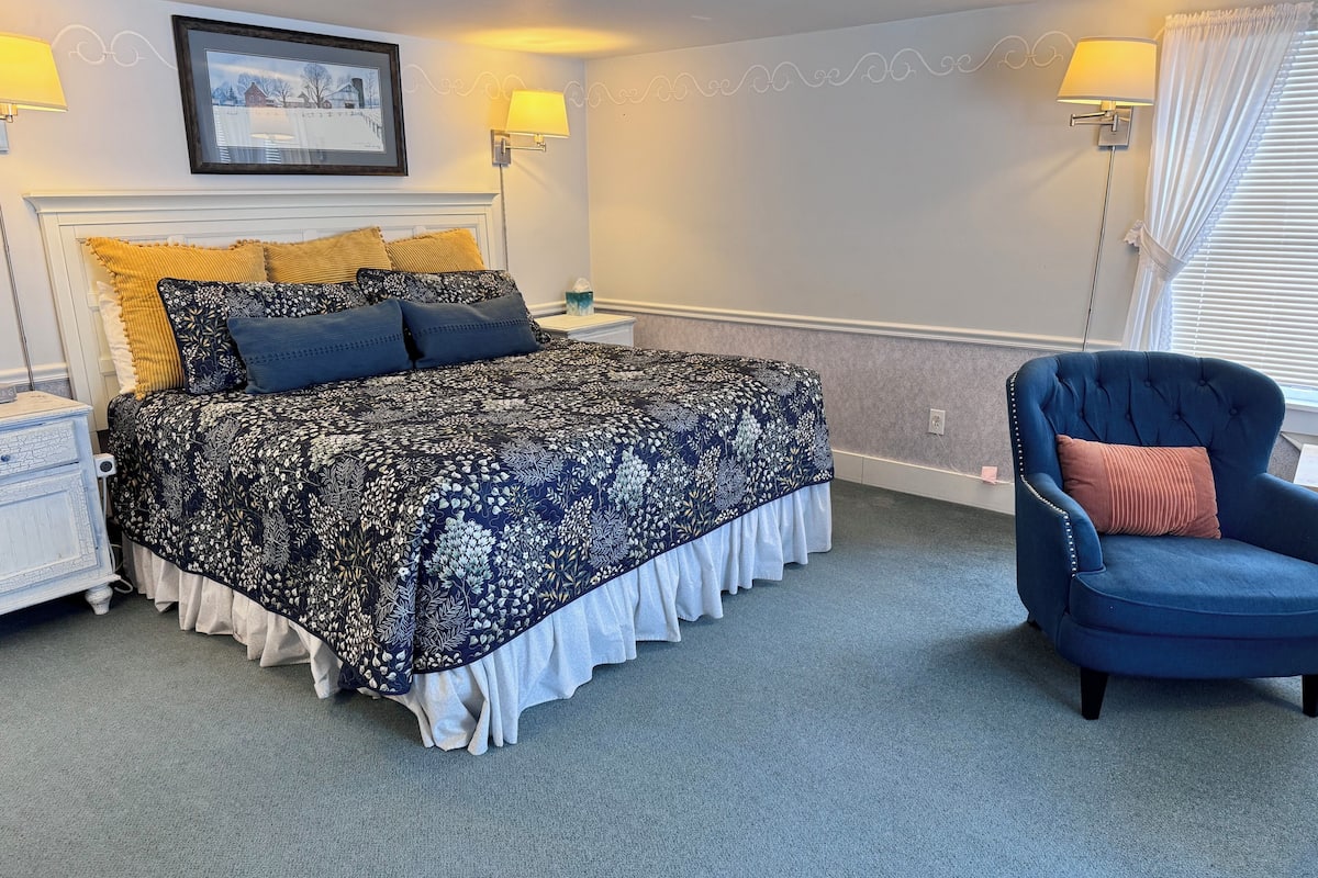 A bedroom with a bed, two bedside lamps, a chair, and a picture on the wall.