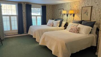 A hotel room with two beds, a window with curtains, a radiator, and a wall with floral wallpaper.