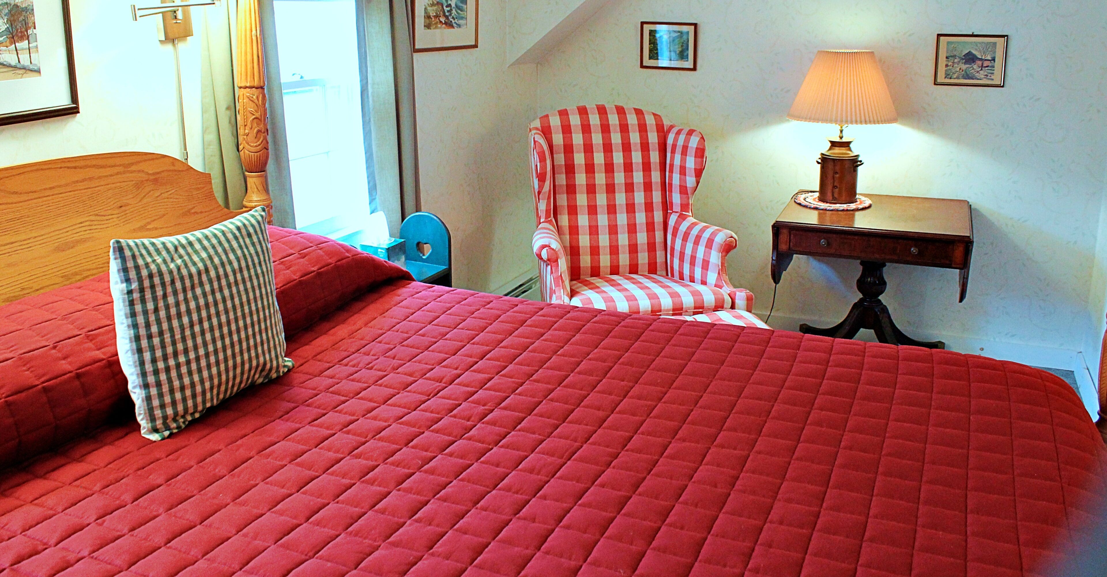 Habitación de hotel con una cama grande, un sillón a cuadros, una mesita de noche con una lámpara y un cuadro en la pared.