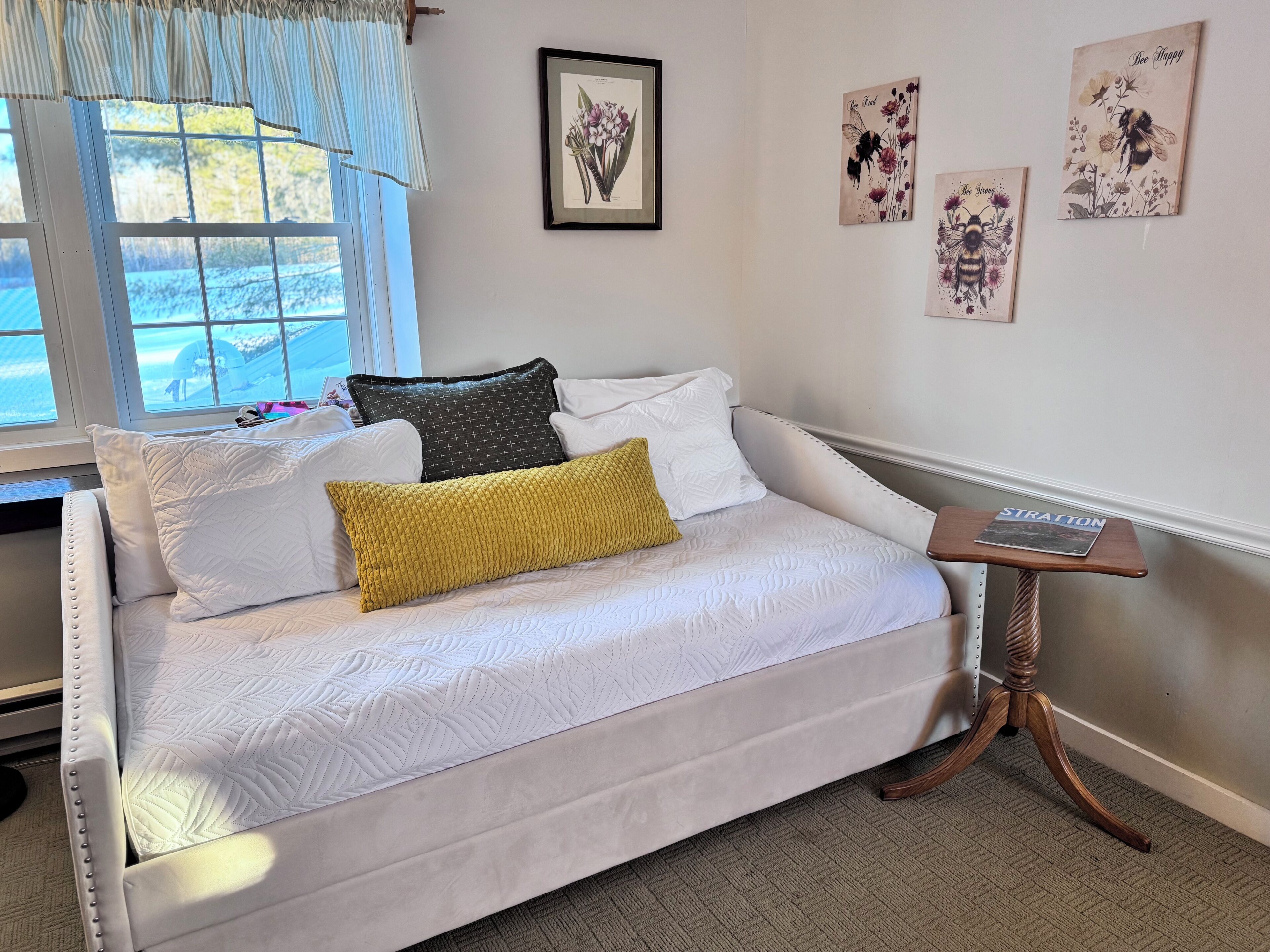 A white sofa with patterned cushions, a small wooden side table, and wall art.