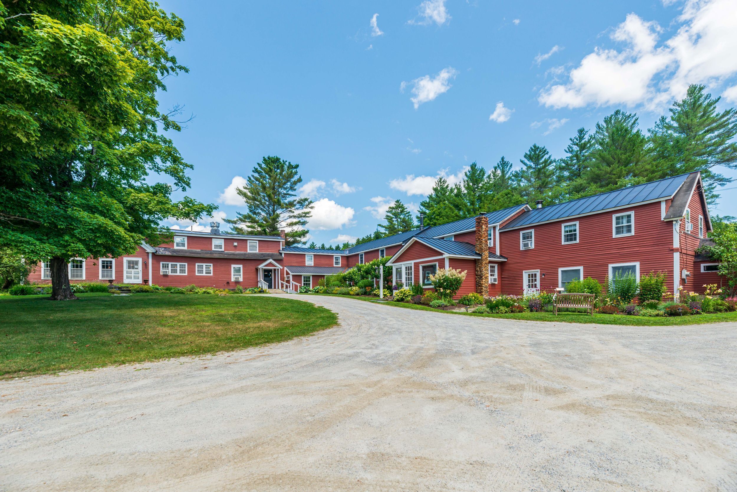 A red building with a gravel driveway and a large tree.