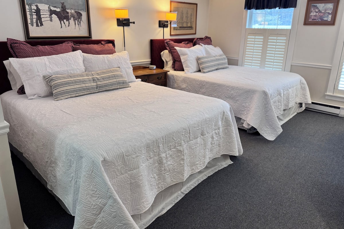 A hotel room with two beds, a nightstand, wall-mounted lamps, and framed artwork.