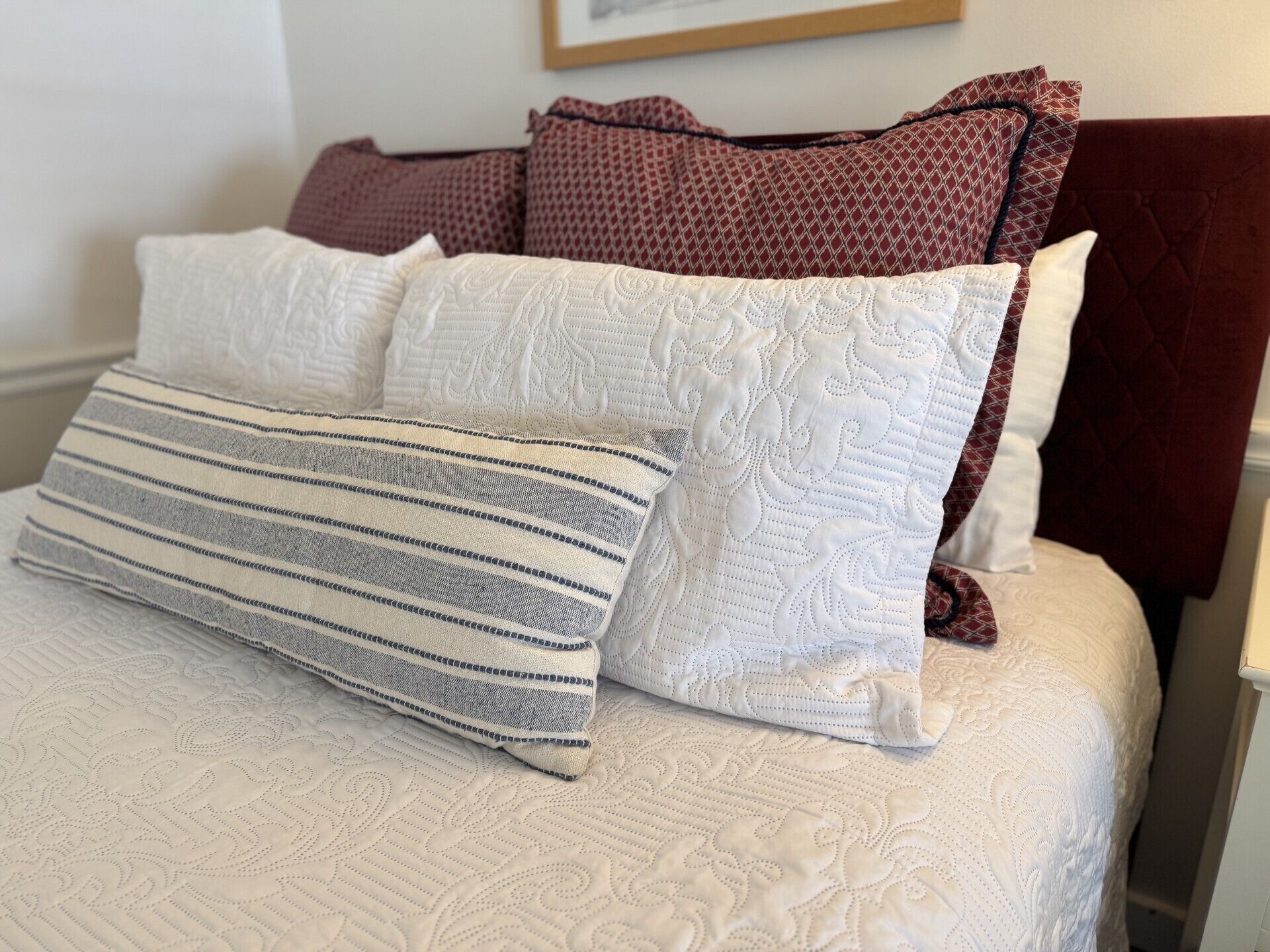 A bed with a white textured bedspread and multiple pillows, including a striped one.