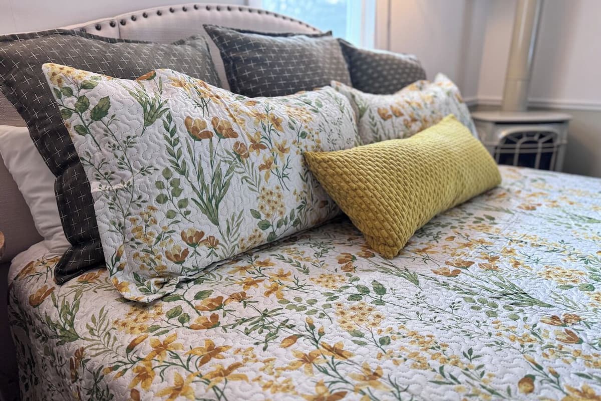 A bed with floral bedding, multiple pillows, and a knitted throw.