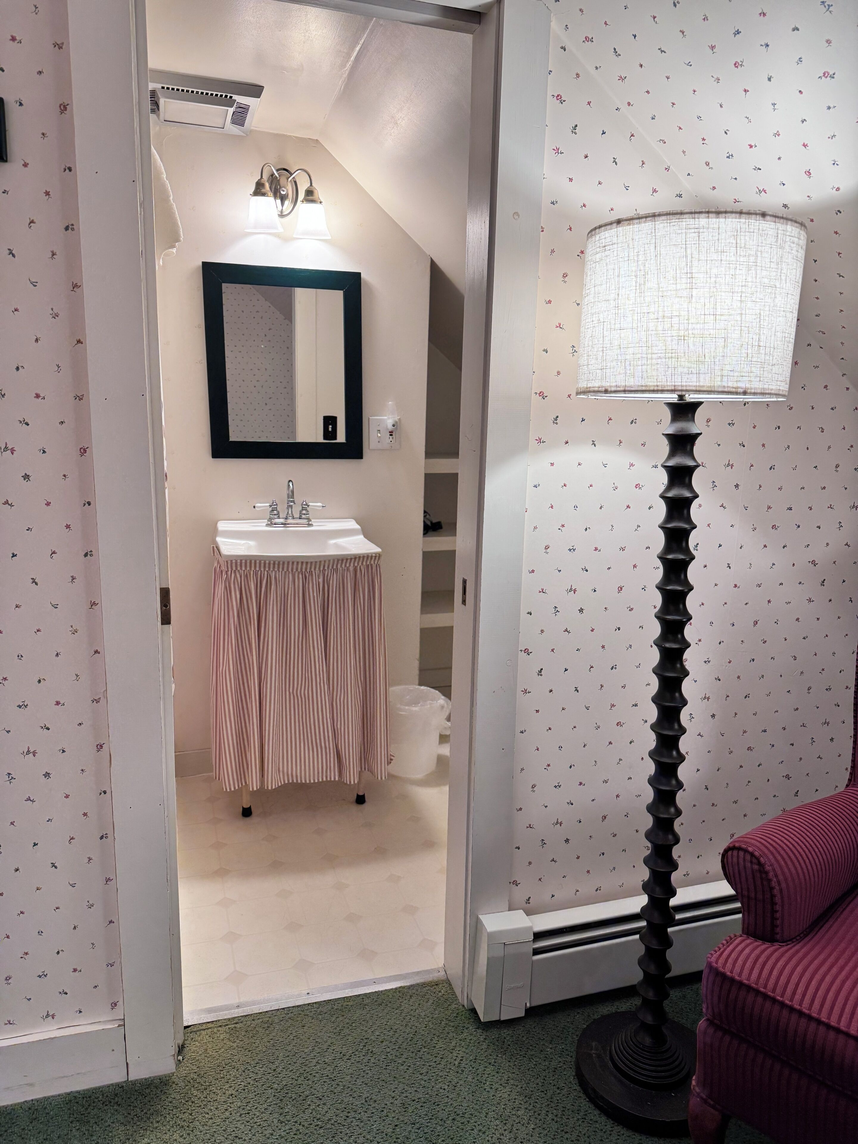 A bathroom with a sink, mirror, and a standing lamp.