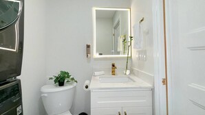 A compact bathroom with a toilet, sink, and mirror. - Designer 4BR Basement Suite – Oakville (Oakville)
