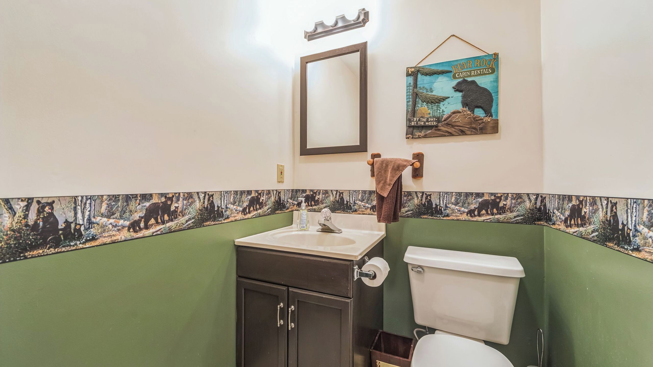A bathroom with a green wall, a sink, a toilet, a mirror, and a bear-themed poster.