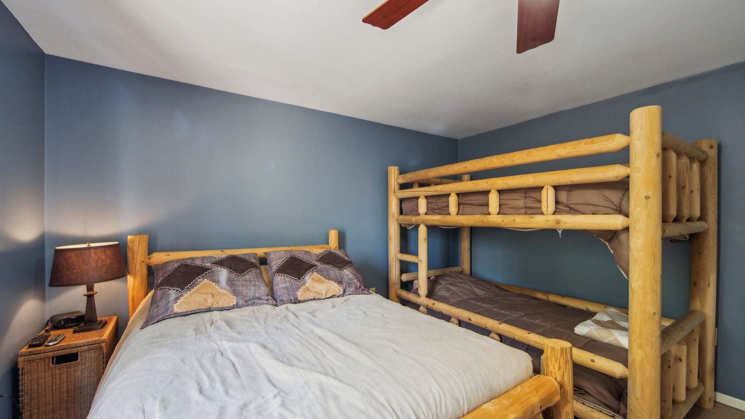 A bunk bed room with a nightstand, lamp, and a ceiling fan.