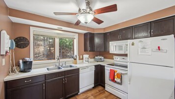 A kitchen with dark wooden cabinets, a white refrigerator, a microwave, a stove, a sink, and a ceiling fan.