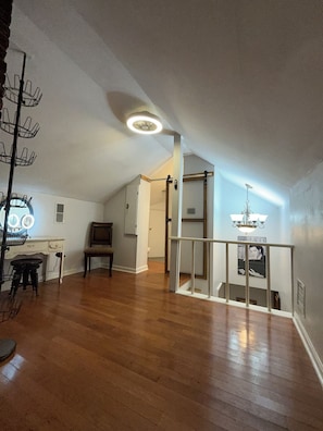 Ein geräumiges Loft mit Holzdielen, einem Essbereich mit Tisch und Stühlen, einer Treppe und einem Deckenventilator.