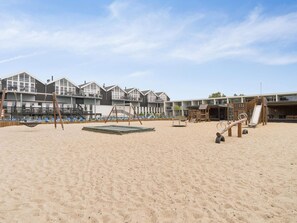 A beach with a swing set, a slide, and a play area. There are buildings in the background. - 5 Star Holiday Home in Glesborg (Glesborg)