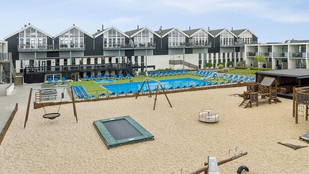 Een hotel met een zwembad, een strandgedeelte en meerdere balkons.