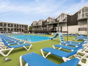 A pool area with blue lounge chairs, a slide, and a building with multiple balconies. - 5 Star Holiday Home in Glesborg (Glesborg)
