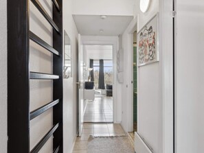 A hallway with a black-framed door, a white wall with a framed picture, and a tiled floor leading to a room with a sofa and a table. - 5 Star Holiday Home in Glesborg (Glesborg)