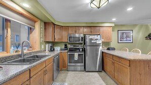 A kitchen with wooden cabinets, stainless steel appliances, a granite countertop, and a window with blinds. - Otterslide by Avantstay Heated Pool + Game Room Near Gore Mtn (North Creek)