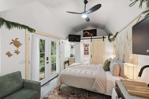 A bedroom with a bed, a green sofa, a ceiling fan, a TV, and a large window.