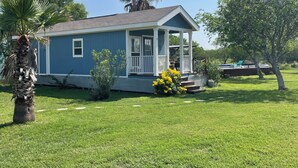 A small blue house with a porch, surrounded by grass and trees.
