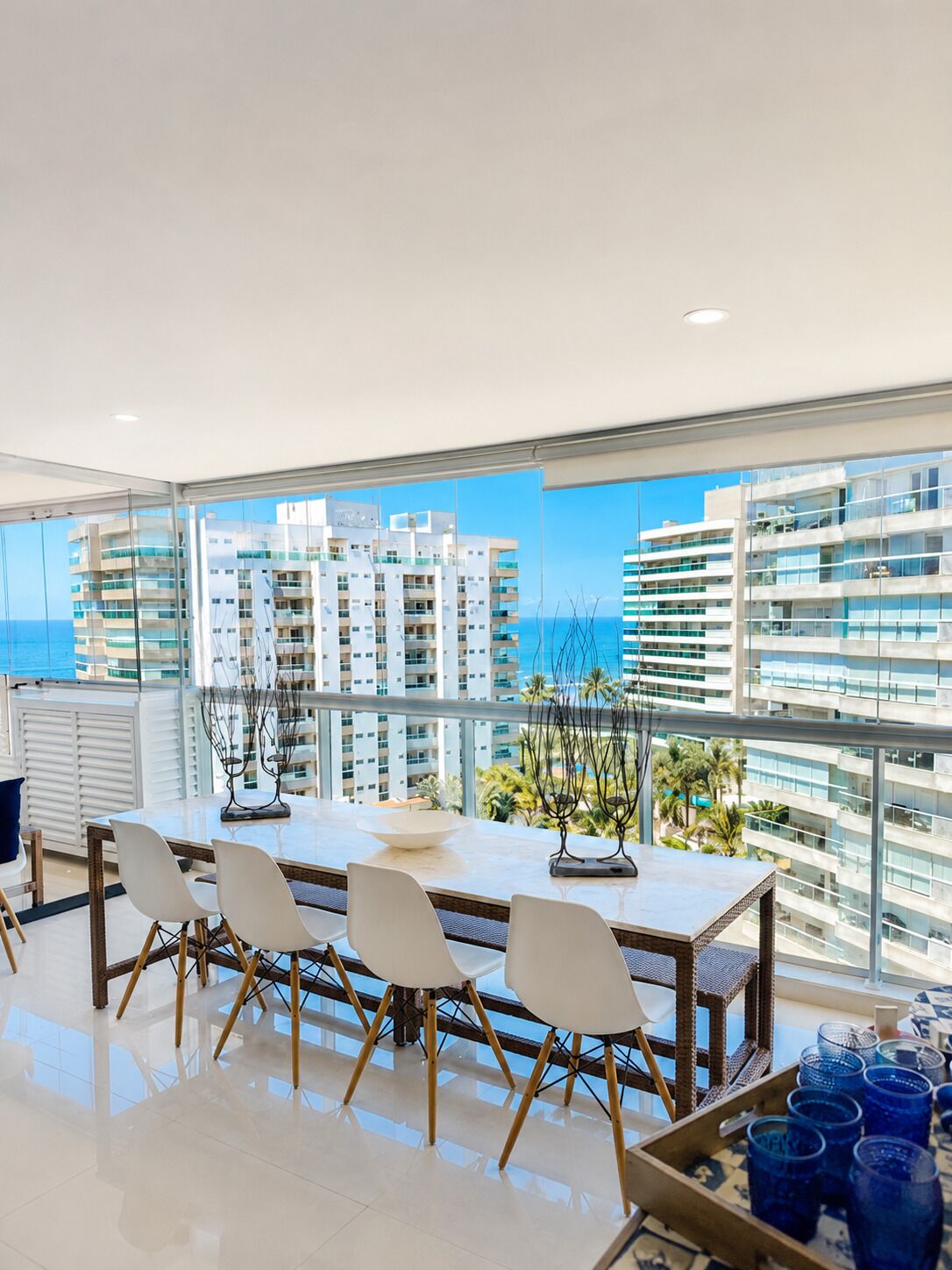 Un espace de restauration moderne avec une table en verre, des chaises blanches et une vue sur les gratte-ciel et la mer.