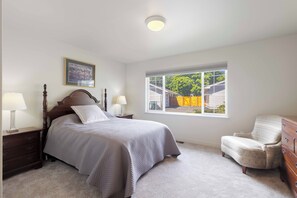 A bedroom with a bed, a chair, a dresser, a nightstand, a window, and a ceiling light.