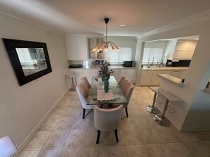 A modern kitchen with white cabinets, a dining table with chairs, and a pendant light. - Peaceful 2-Bedroom Condo in Sunny La Jolla (San Diego)