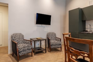 A modern kitchen with a flat-screen TV, two patterned armchairs, a small table, and a wooden dining table. - Coronari 6 - FromHometoRome (Roma)