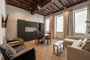 A living room with a sofa, a dining table with chairs, a kitchen area with cabinets, and large windows with curtains. - Coronari 6 - FromHometoRome (Roma)