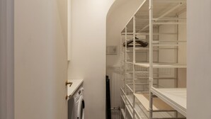 En smal gang med en vaskemaskine, en radiator og en hvid reol med bøjler.