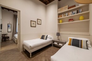A hotel room with two beds, a small table, a shelf with books and decorative items, and a door leading to another room. - Coronari 6 - FromHometoRome (Roma)