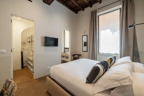 Ein Schlafzimmer mit einem Bett, einem an der Wand montierten Fernseher, einem Fenster mit Vorhängen und einem Kleiderschrank mit Regalen.