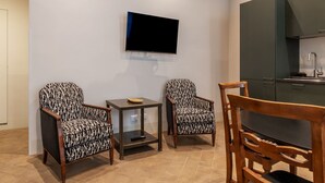 Et moderne køkken med et fladskærms-tv, to mønstrede lænestole, et lille bord og et træspisebord.