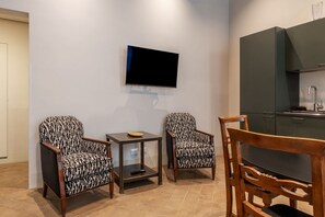 Eine moderne Küche mit Flachbildfernseher, zwei gemusterten Sesseln, einem kleinen Tisch und einem Holzessttisch.