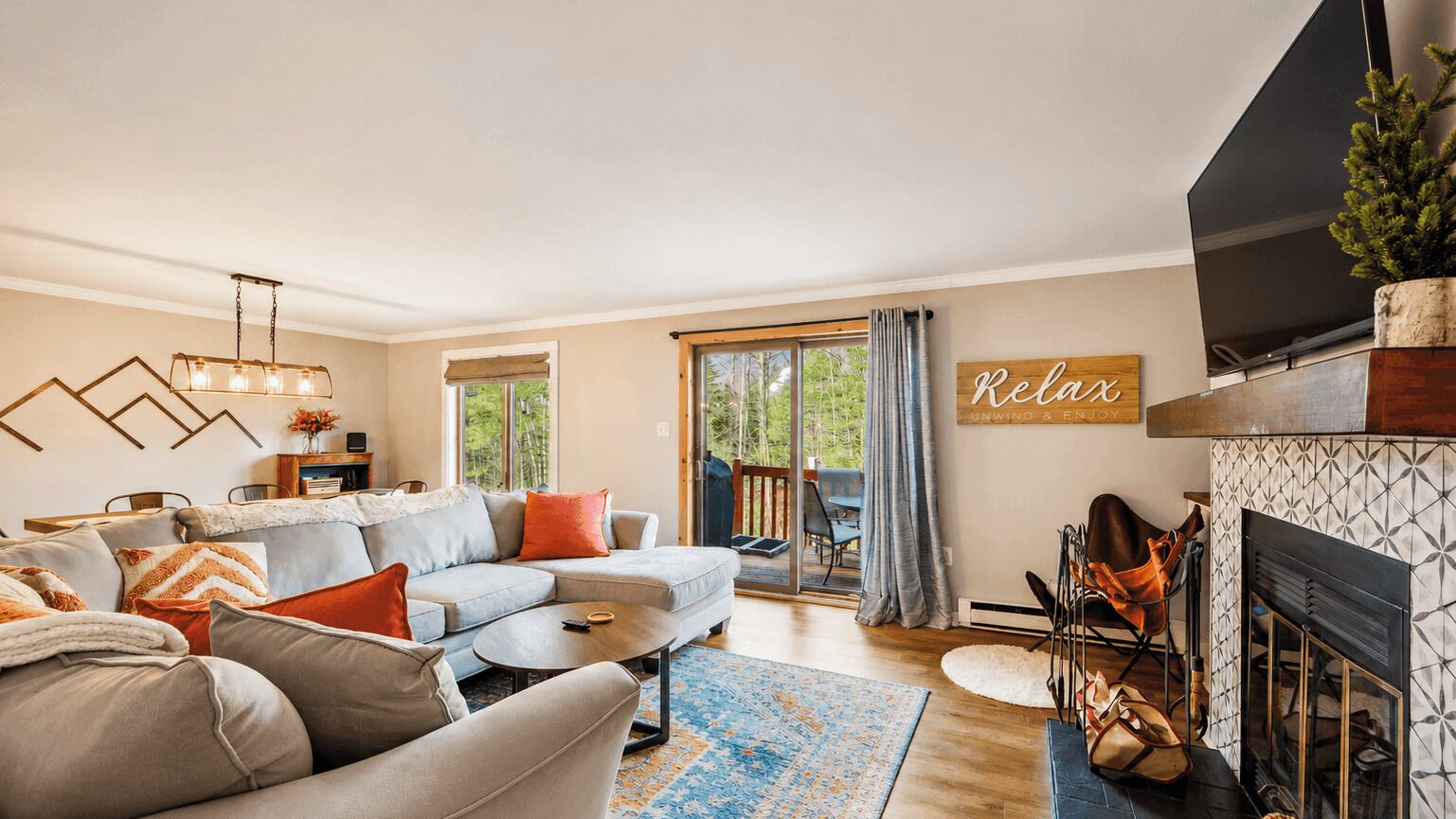 A living room with a sectional sofa, a fireplace, a television, and a large window with curtains.