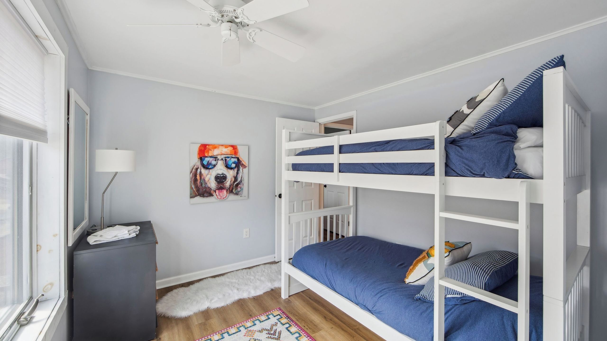 A bunk bed room with a ceiling fan, a painting, a desk, and a window.