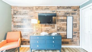 Una habitación con paneles de madera, un televisor de pantalla plana, un aparador azul y una silla naranja.